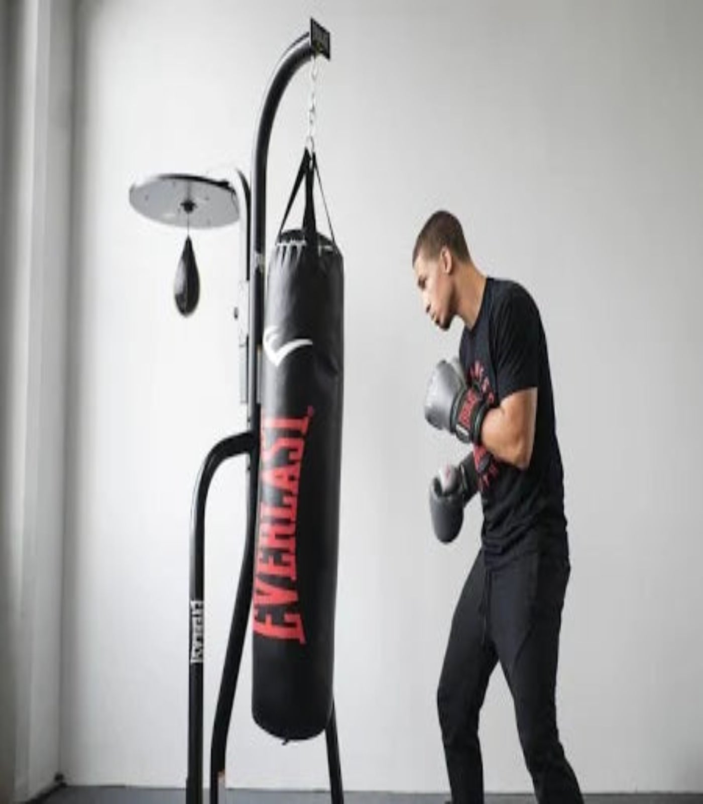Person wearing boxing gloves and punching a Everlast punching bag in a gym setting.