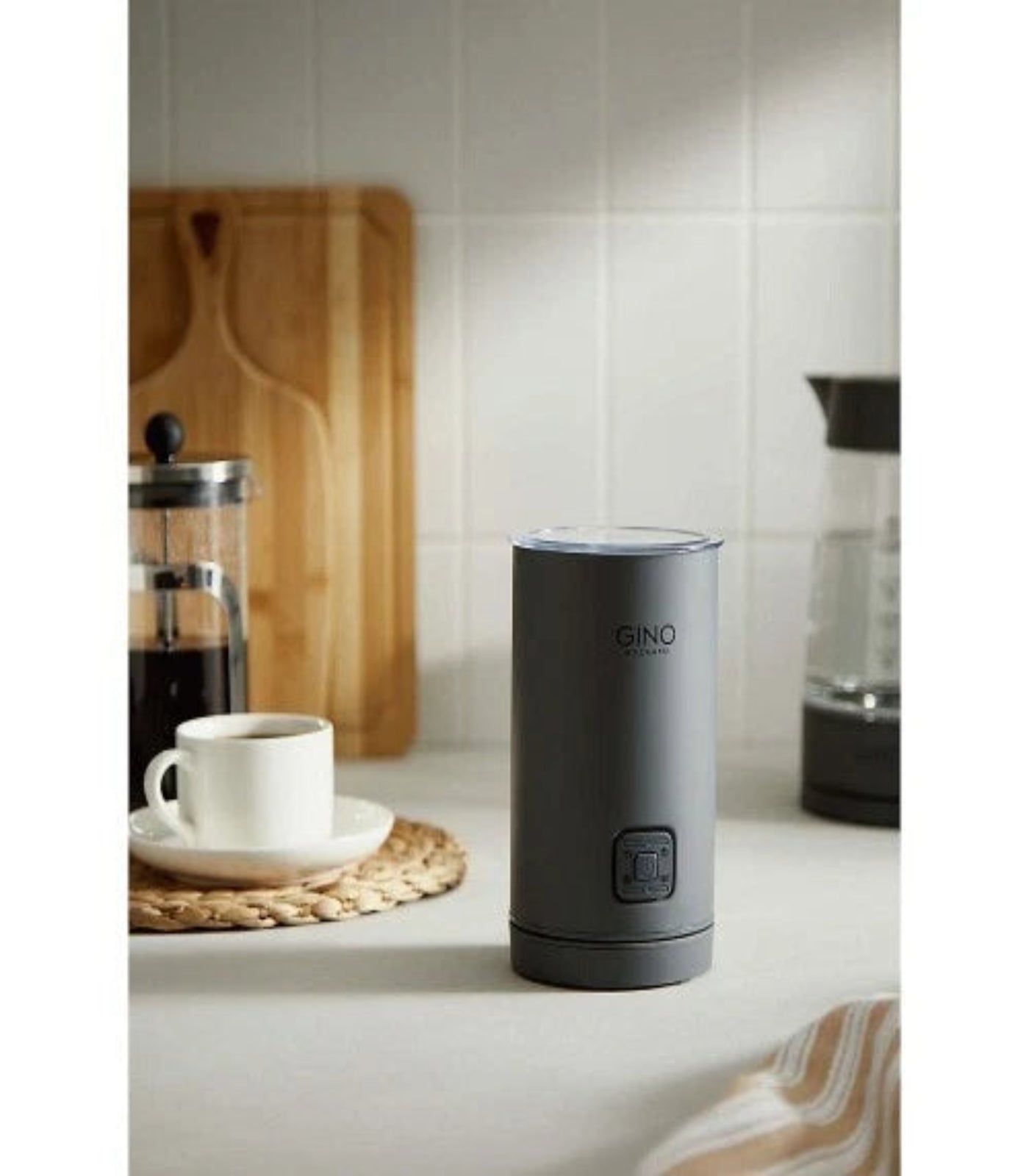 Gray GINO coffee grinder on a kitchen counter with a cup of coffee and a French press in the background.