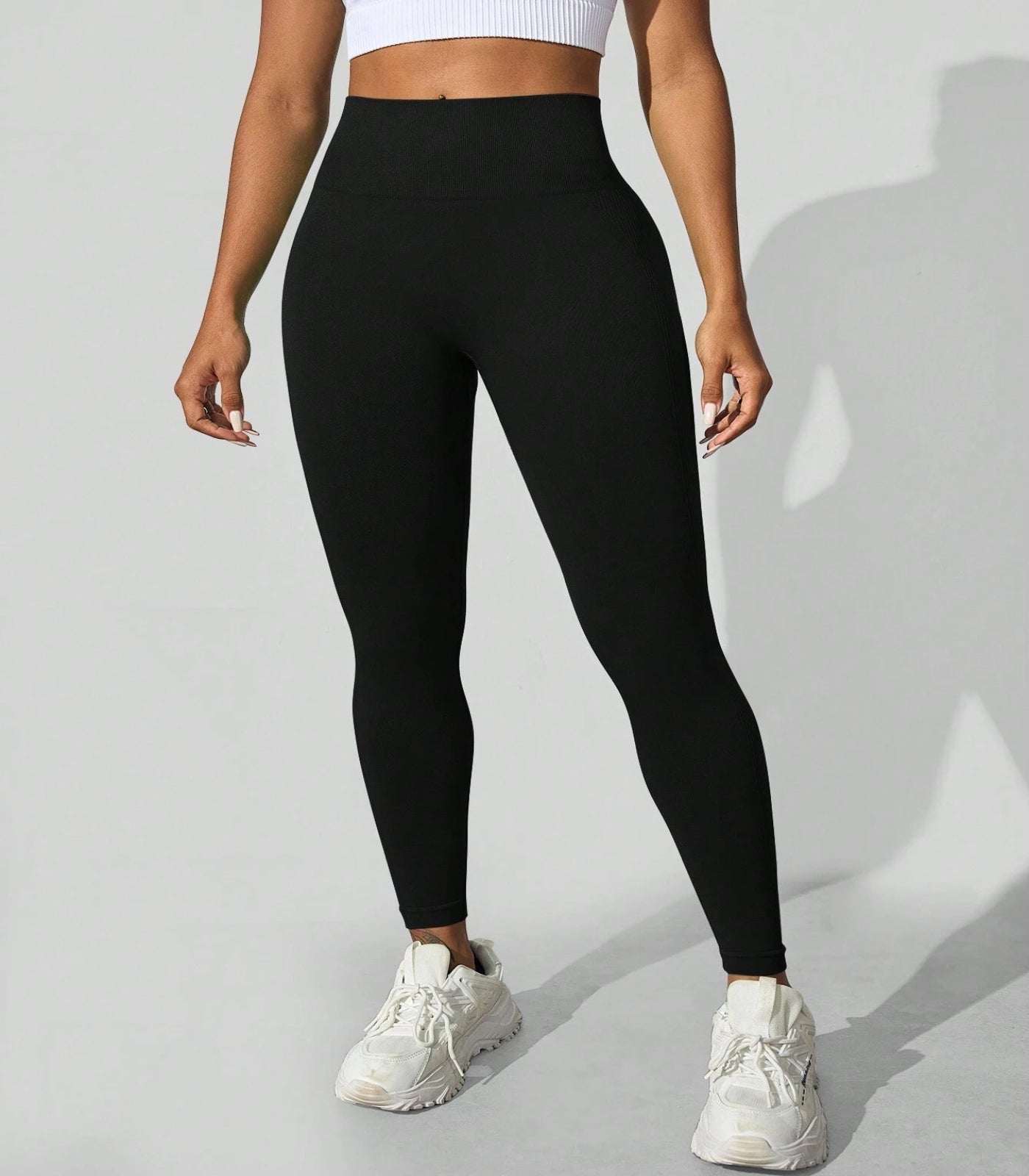 Person wearing black leggings and white sneakers on a light gray background