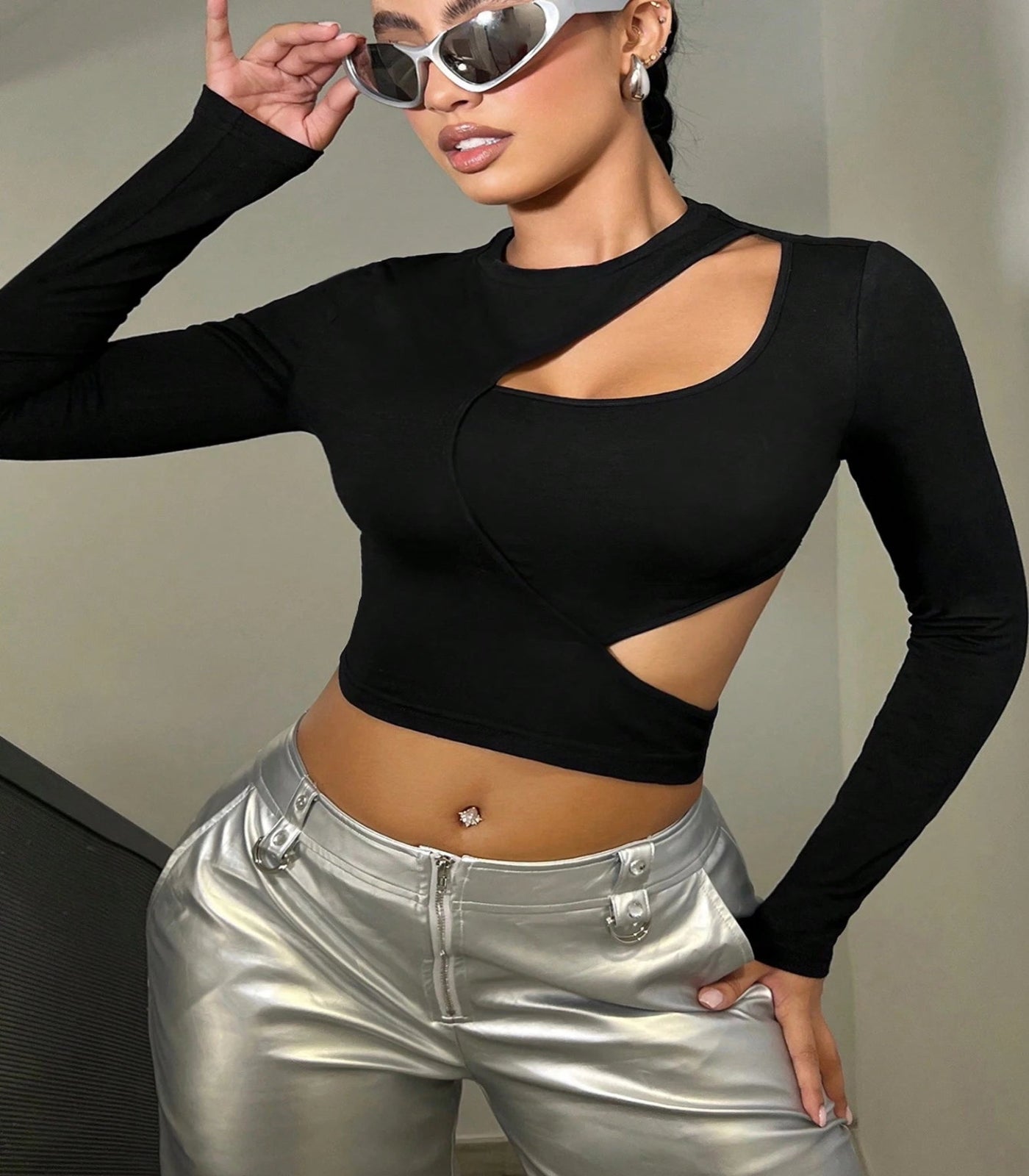 Person wearing a black long-sleeve crop top with cut-out design and silver pants against a neutral background