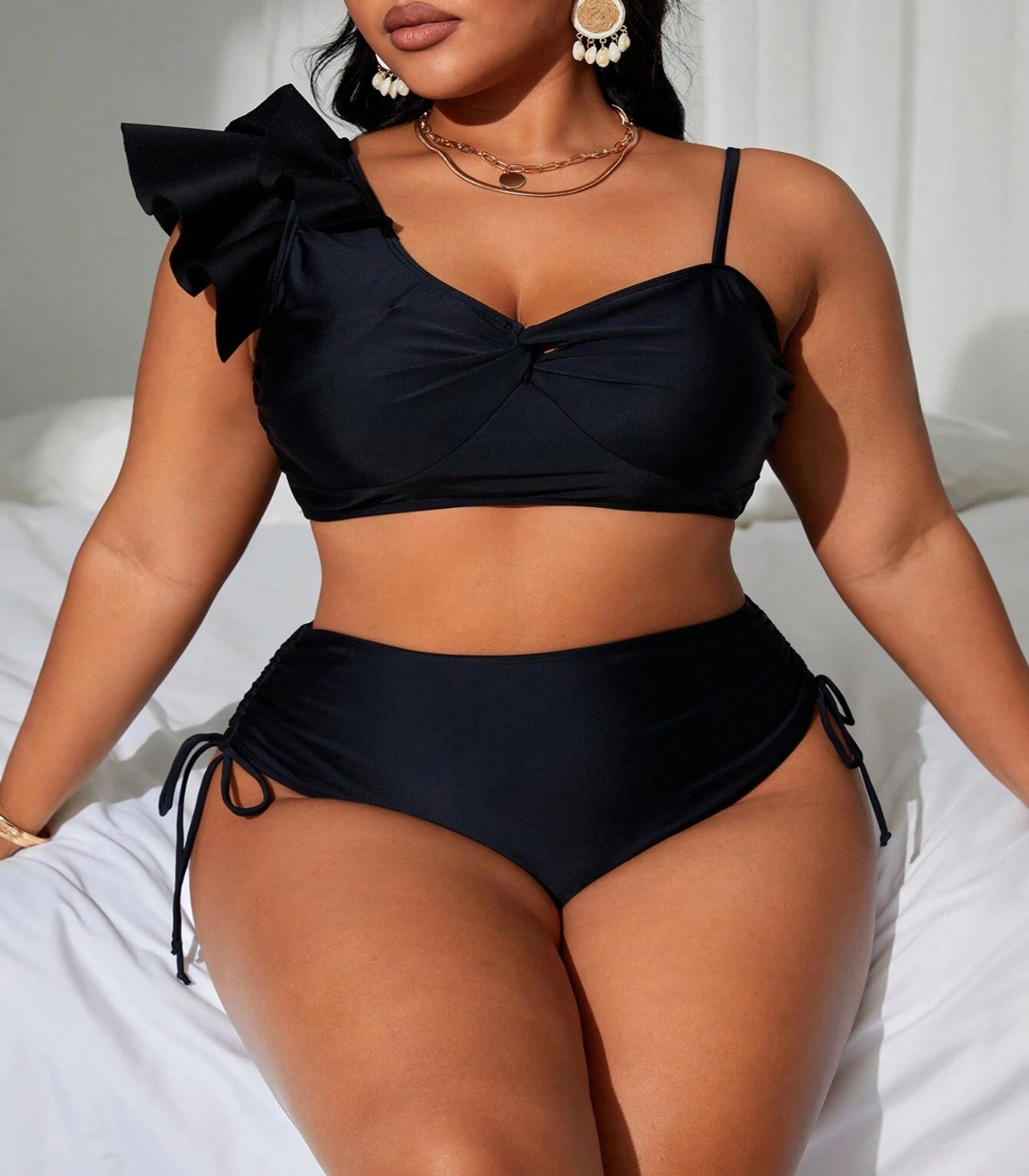 Woman wearing a black bikini with ruffled top and high-waisted bottoms on a white background