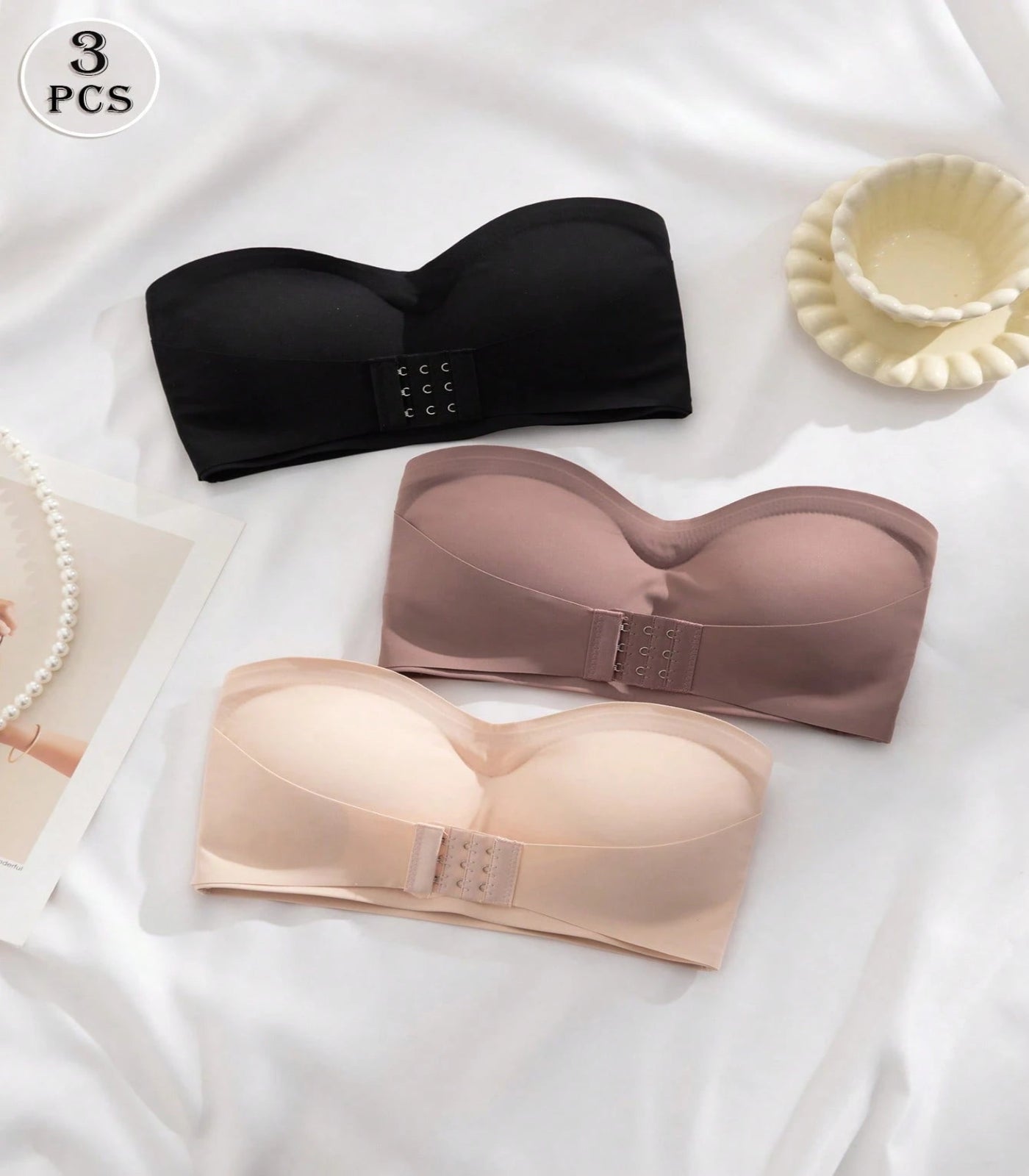 Three black, beige, and pink strapless bras on a white background