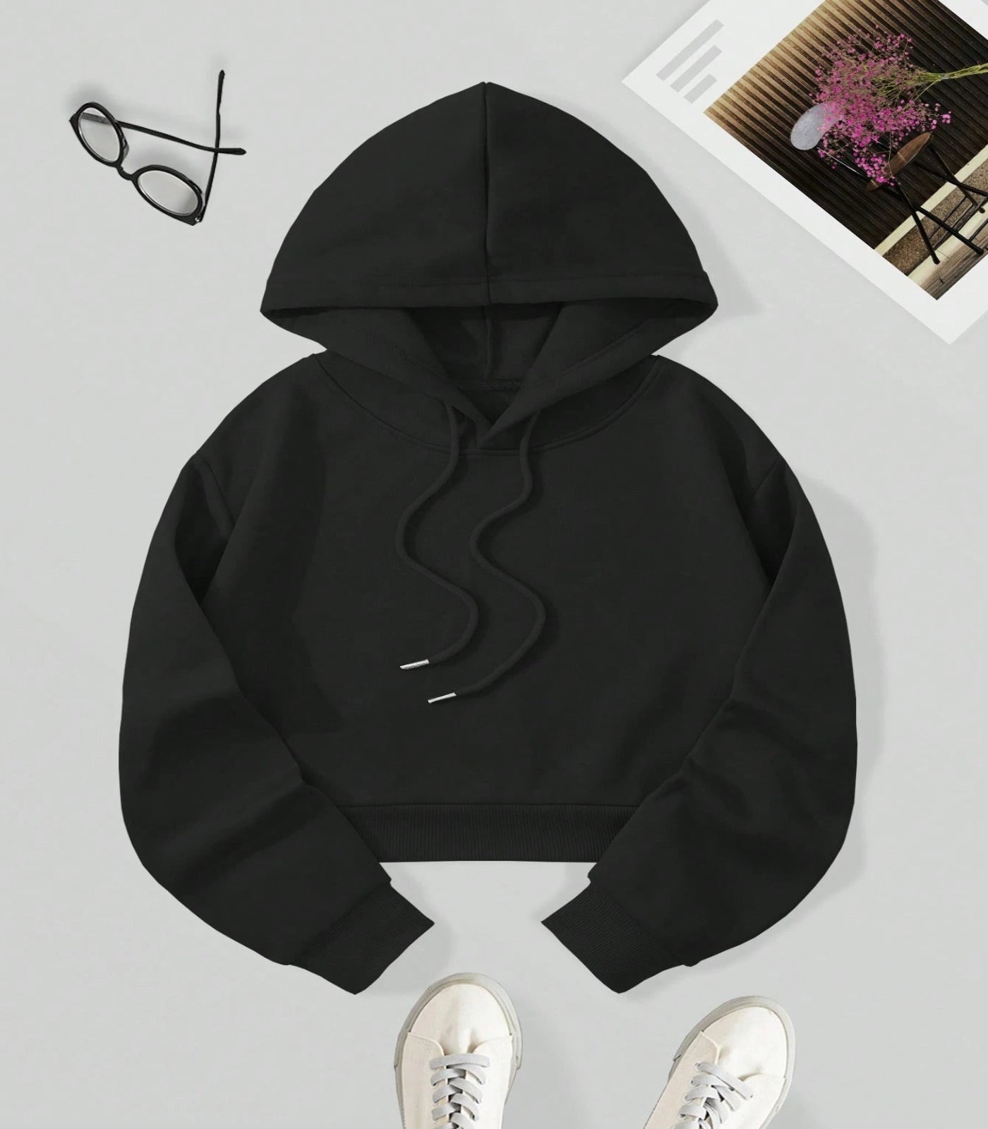 Black hoodie on a light gray surface with glasses and a photo frame in the background.