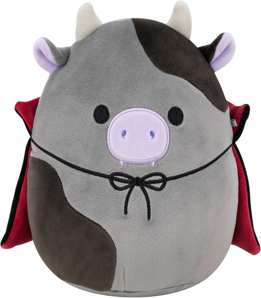 Plush toy resembling a cow with devil horns, tail, and red cape on a white background
